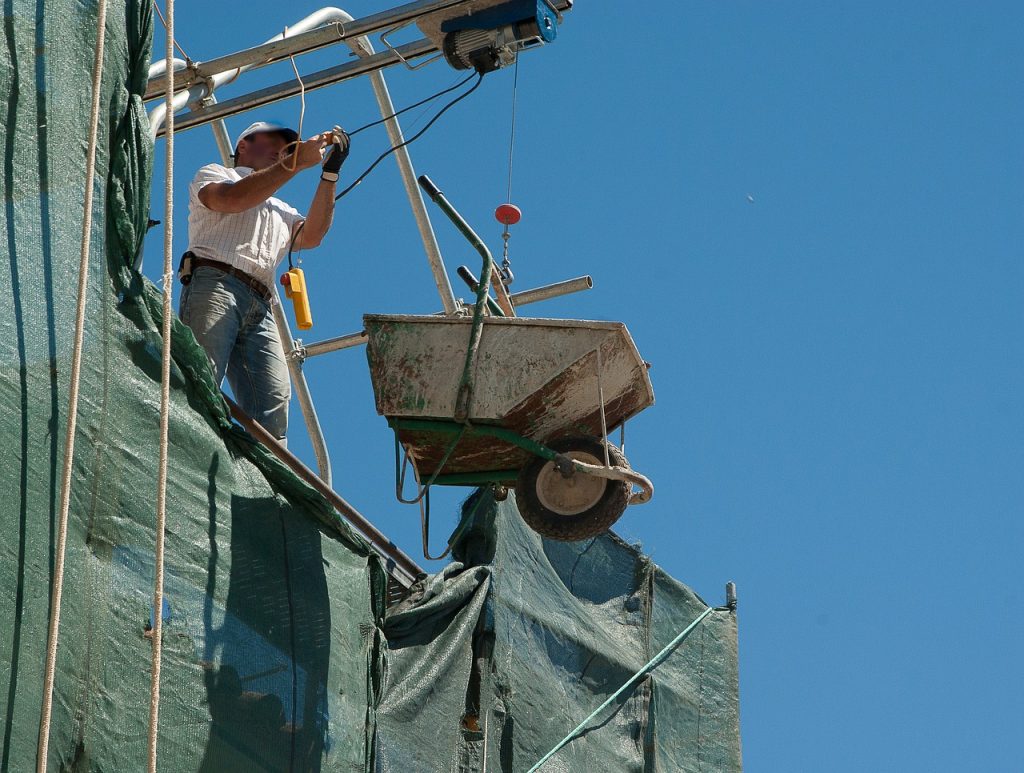ouvrier de chantier qui fait monter une brouette grâce à des poulies
